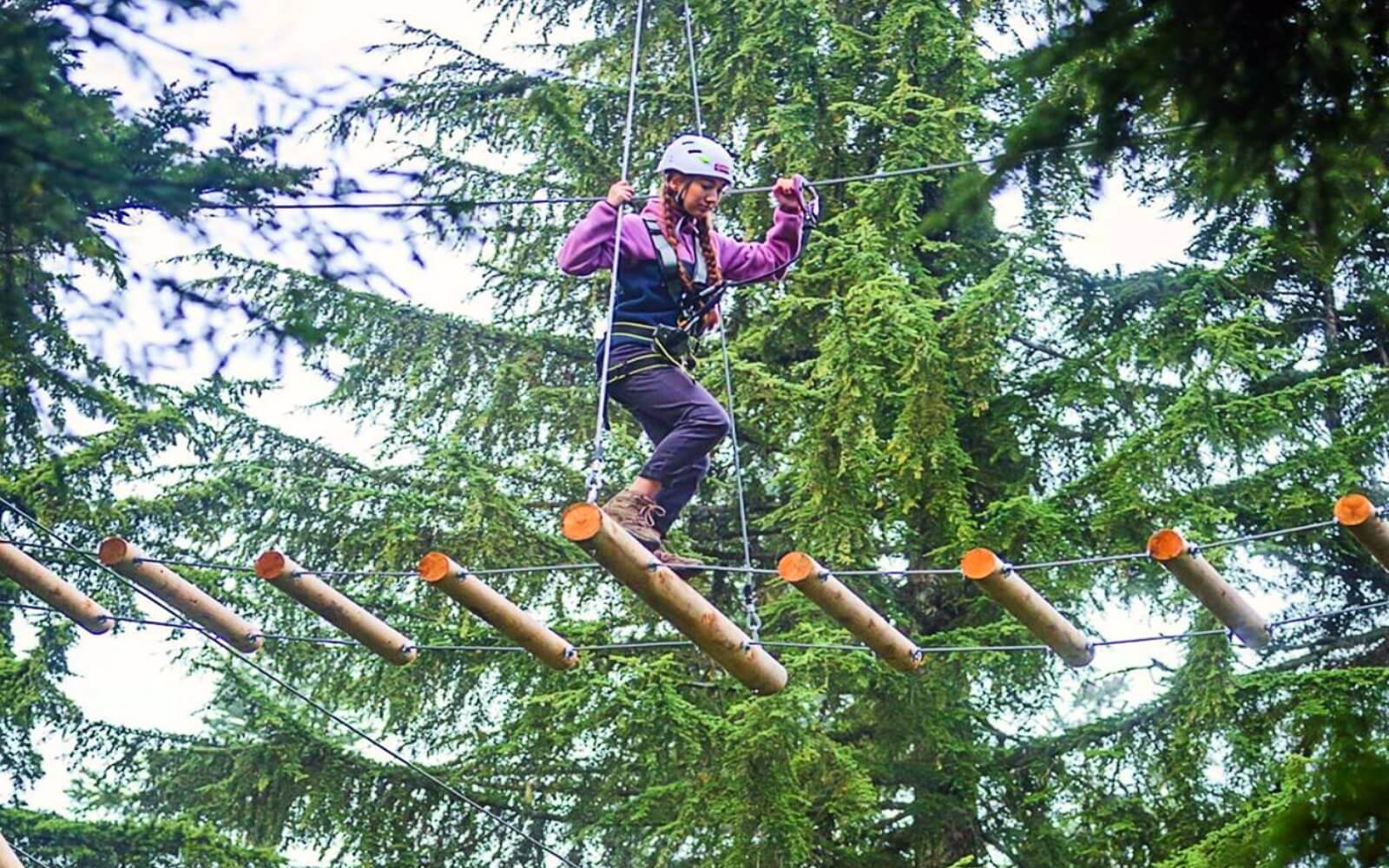 A woman climbs through the forest on a ropes adventure