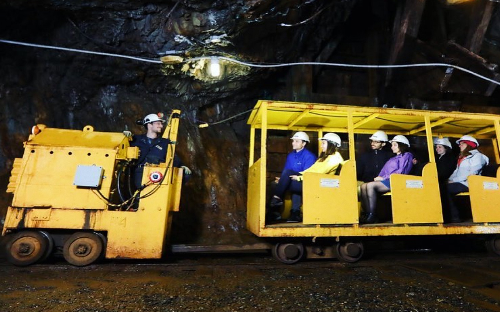 A group of visitors ride an underground train through a mine shaft