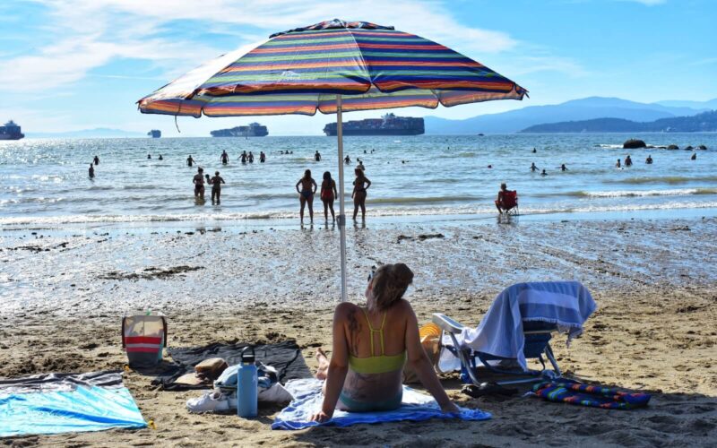 a woman lounging under an umbrella at second beach in vancouver in summer