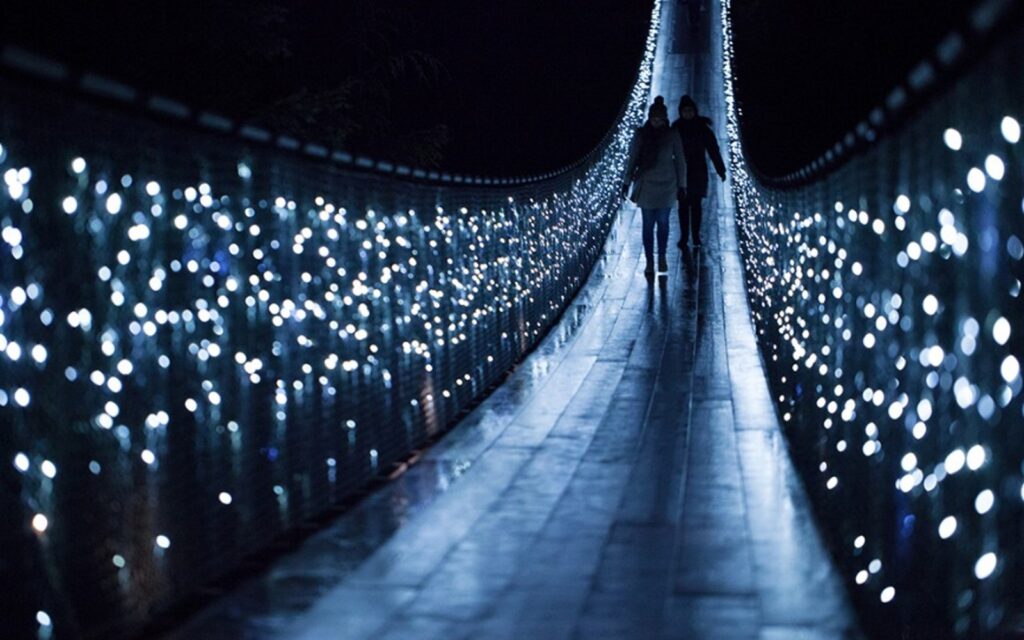 two individuals walking on the capilano suspension bridge during the canyon lights event