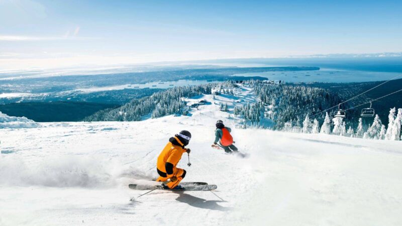 skiers racing down the grouse mountain ski hill with the vancouver harbour in the background