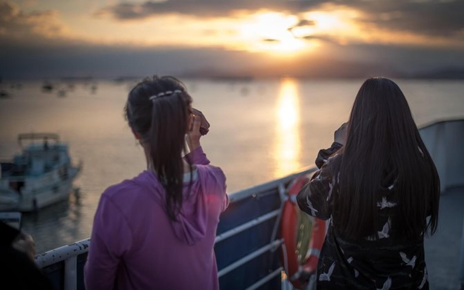 two tourists taking a photograph of the setting sun from a vancouver sunset boat tour