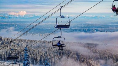 a lone skier on a chairlift with vancouver city view at cypress mountain ski hill