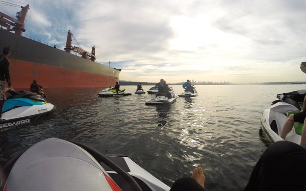 a group cruises past a freighter on an english bay seadoo tour.