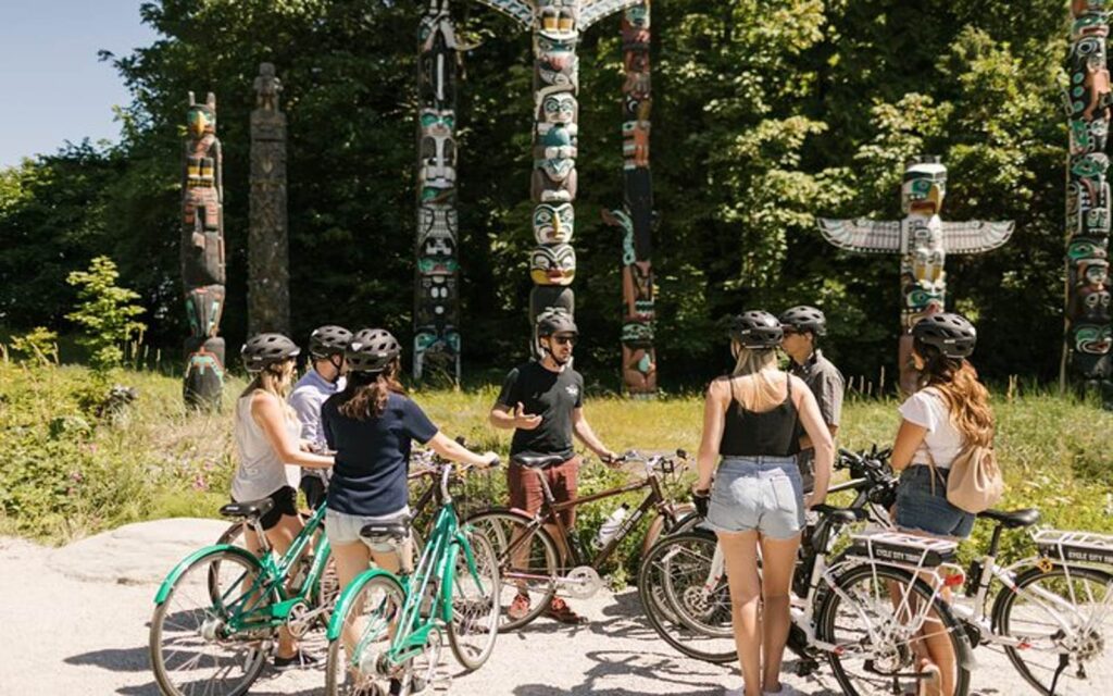 a group bikes past the totem poles on a stanley park tour