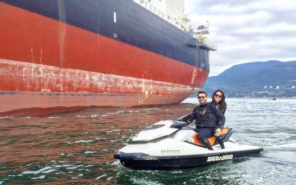 a couple poses next to a freighter on their vancouver jet ski rental.