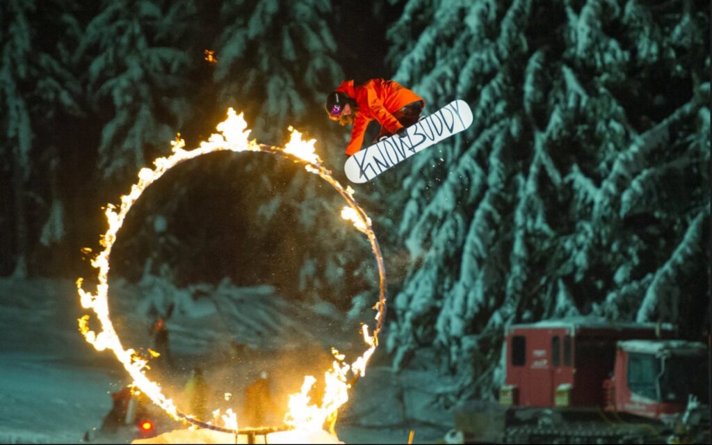 a snowboarder jumps through a ring of fire at the whistler fire and ice festival.