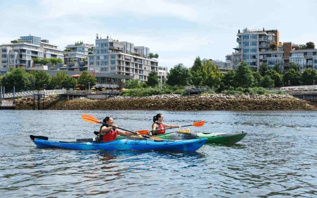 two women kayaking in the middle of false creek with orange paddle and blue boat 