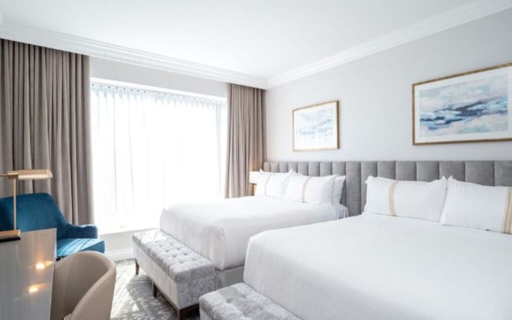 2 queen beds covered in white sheets with the window open at sutton place hotel vancouver