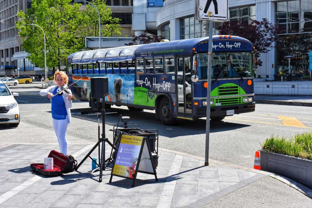 street musician performing in front of the vancouver hop on hop off bus tour
