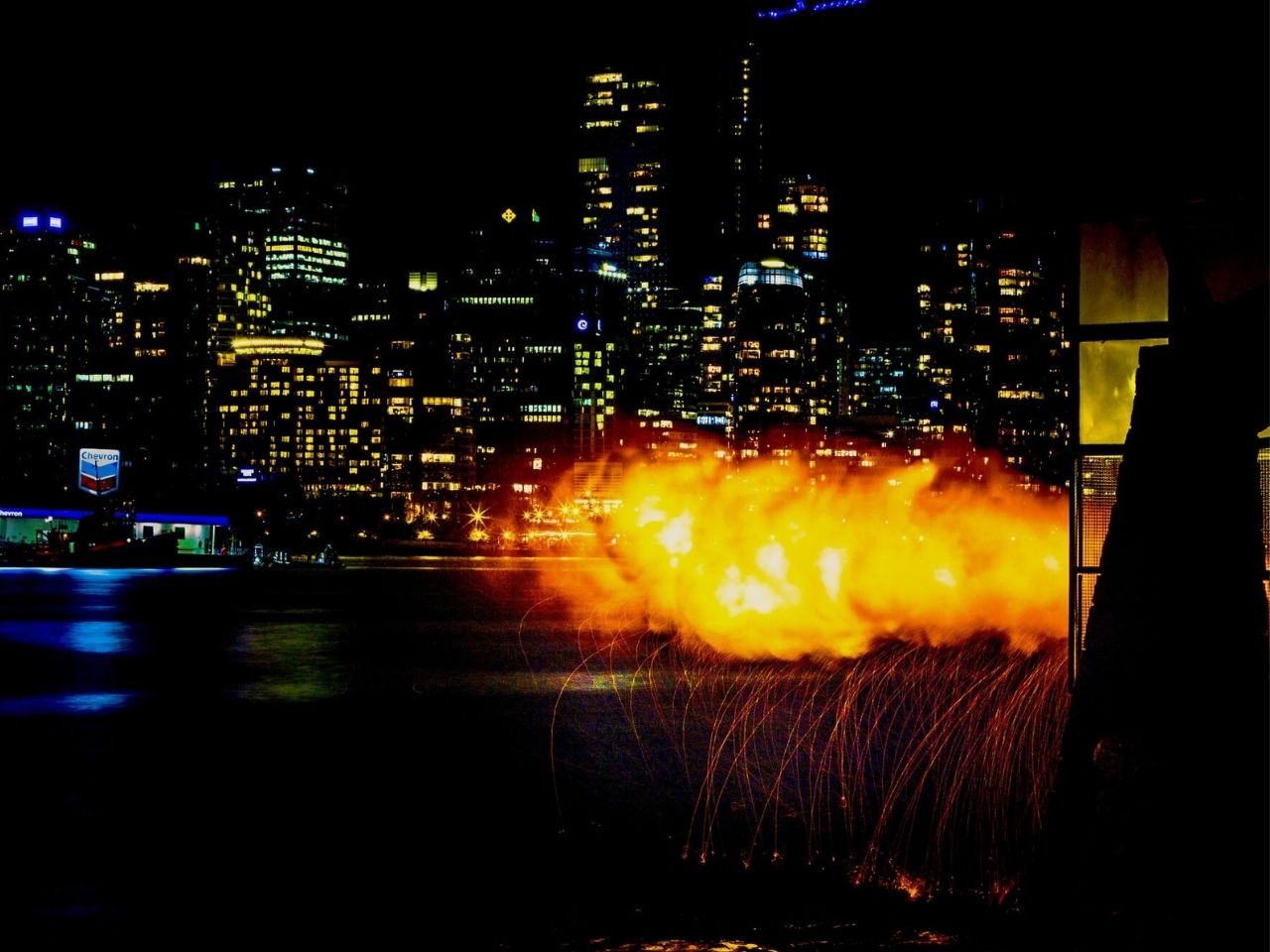 the fiery blast from the 9 o'clock gun against vancouver's illuminated skyline at night