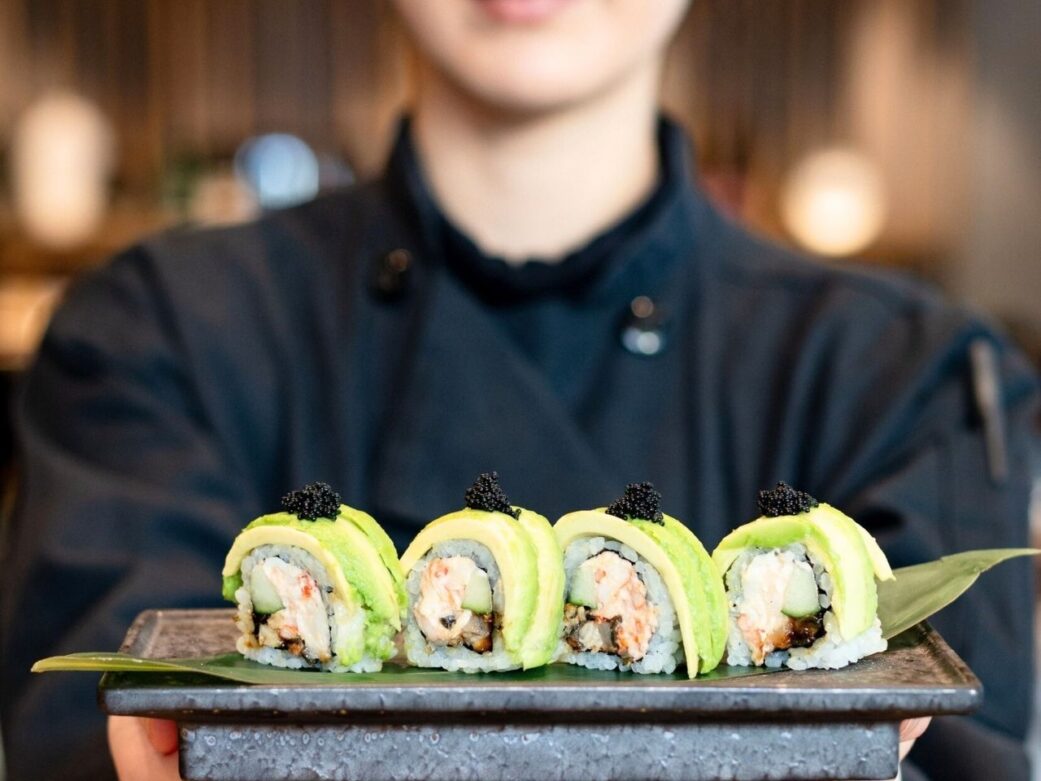 a waitress carrying a plate full of sushi rolls with avocado on top