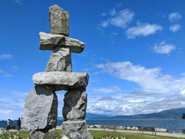 large stone inukshuk sculpture by the waterfront under a blue sky in vancouver