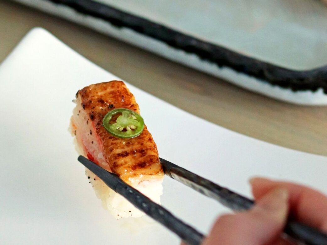 aburi salmon sushi held on chpsticks with green chili on top at miku one of the best sushi restaurants in vancouver