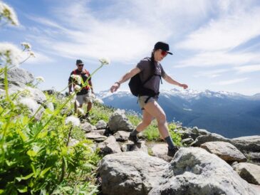 a man and woman hiking up on whistler's mountain during summer with a very beautiful view at the back